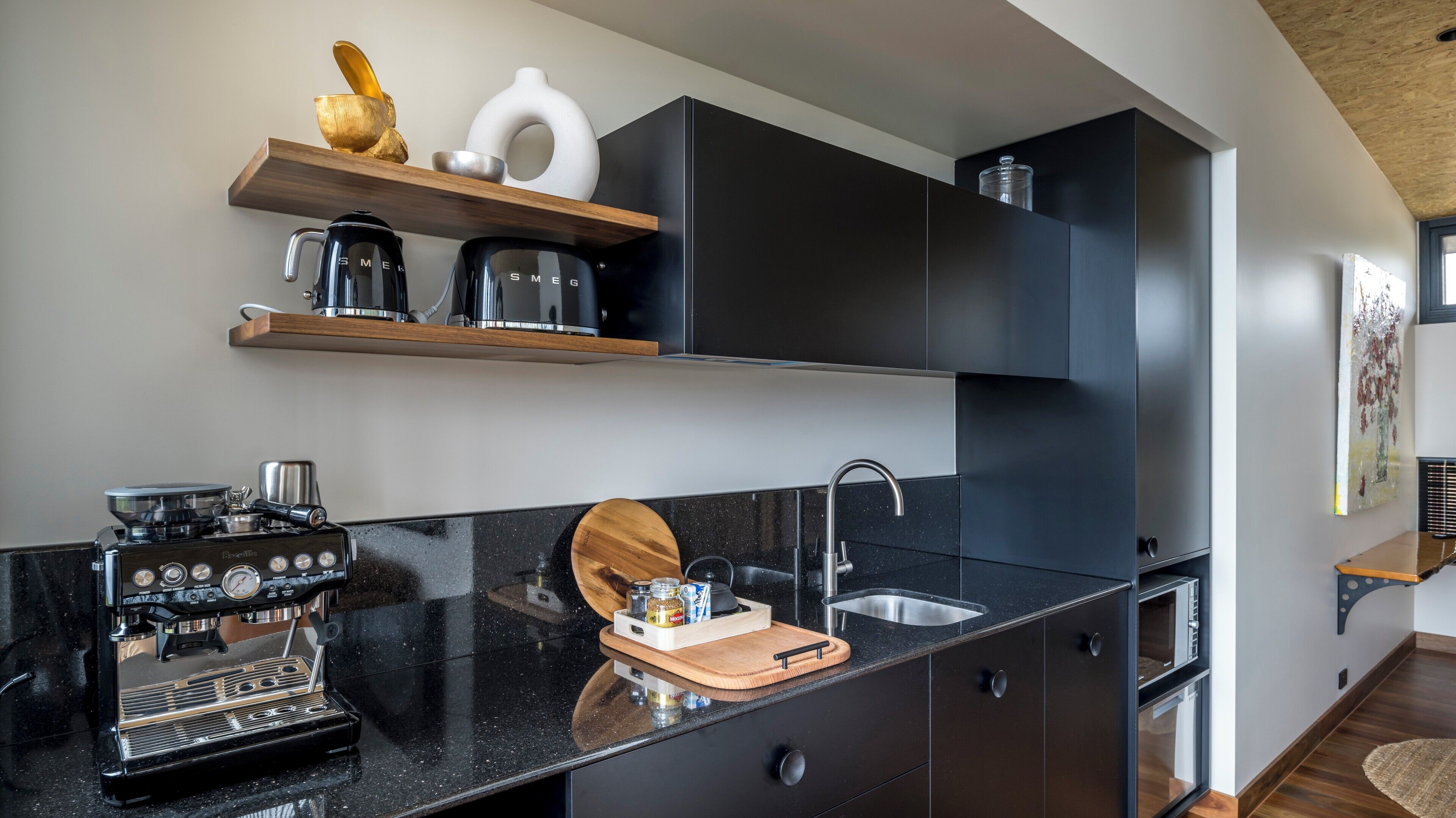 Una cocina moderna con encimera negra, cafetera, fregadero y tabla de cortar de madera.
