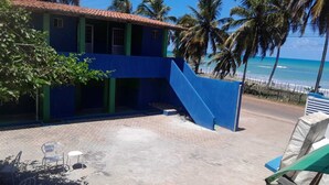A building with a blue exterior, a staircase leading to a balcony, and a view of the beach and ocean. - Pousada da Kika  (Touros)