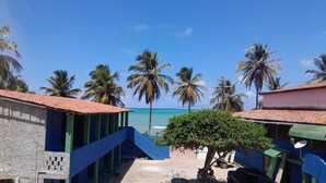A coastal building with a staircase leading to a beach, surrounded by palm trees and a clear blue sky. - Pousada da Kika  (Touros)