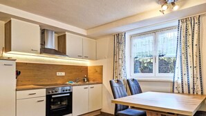 A modern kitchen with wooden cabinets, a built-in oven, and a dining area with a table and chairs. - Cosy apartment for 4 guests with WIFI, TV and terrace (Wenns)