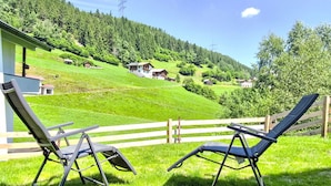 A terrace with two lounge chairs overlooking a green hillside with houses and a power line tower. - Cosy apartment for 4 guests with WIFI, TV and terrace (Wenns)