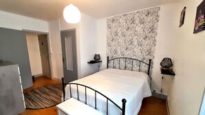 Et soveværelse med seng, natbord, lampe, dør og et lille bord.