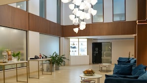Un hall d’entrée spacieux avec un plafond haut, un espace de détente central agrémenté de canapés bleus, un comptoir d’accueil et une grande fenêtre où sont exposés les produits.