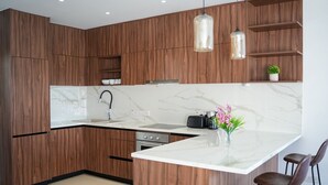 Une cuisine moderne avec des armoires en bois, un comptoir en marbre, un four encastré et des luminaires suspendus.