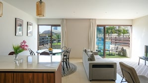 Un salon moderne comprenant un coin repas, un canapé et un téléviseur. Une grande fenêtre offre une vue sur une piscine et sur la verdure environnante.