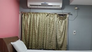 A room with a bed, a window with a curtain, an air conditioning unit, and a wall socket. - Elite Residency Pallavaram (Chennai)