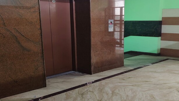An elevator in a hallway with a marble floor and a green wall. - Elite Residency Pallavaram (Chennai)