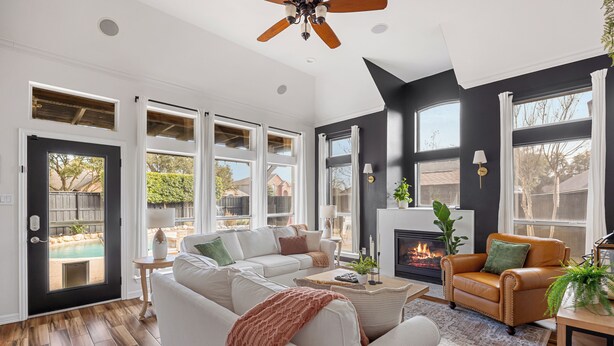 A spacious living room with a white sofa, a leather armchair, and a fireplace. Large windows provide natural light and views of the outdoors. - Resort-style, Frisco Getaway, Saltwater Pool, FREE Heated Spa (Frisco)