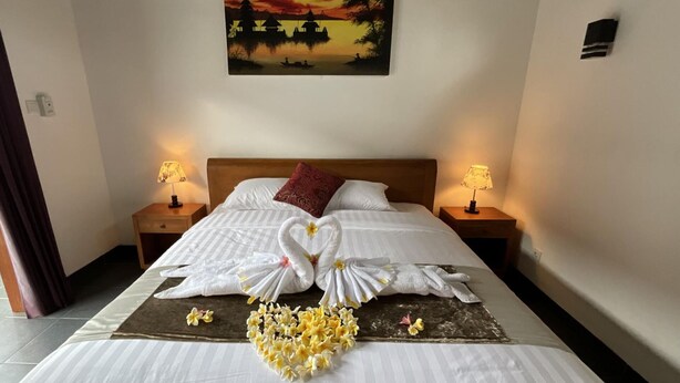 A hotel room with a bed, two bedside tables, a painting of a sunset, and a floral arrangement on the bed. - Villa - Sleeps 6 - Private pool - Parking (Karangasem)