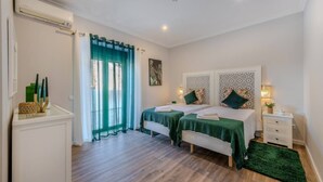 A bedroom with two beds, a large window with sheer curtains, a bedside table with a lamp, and a small bedside table with a plant. - Quinta Ribeira do Arade (São Bartolomeu de Messines)