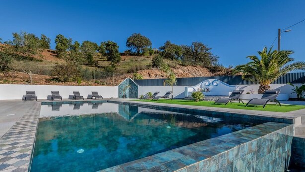 A rectangular swimming pool with a tiled edge, surrounded by lounge chairs and a small garden area. - Quinta Ribeira do Arade (São Bartolomeu de Messines)