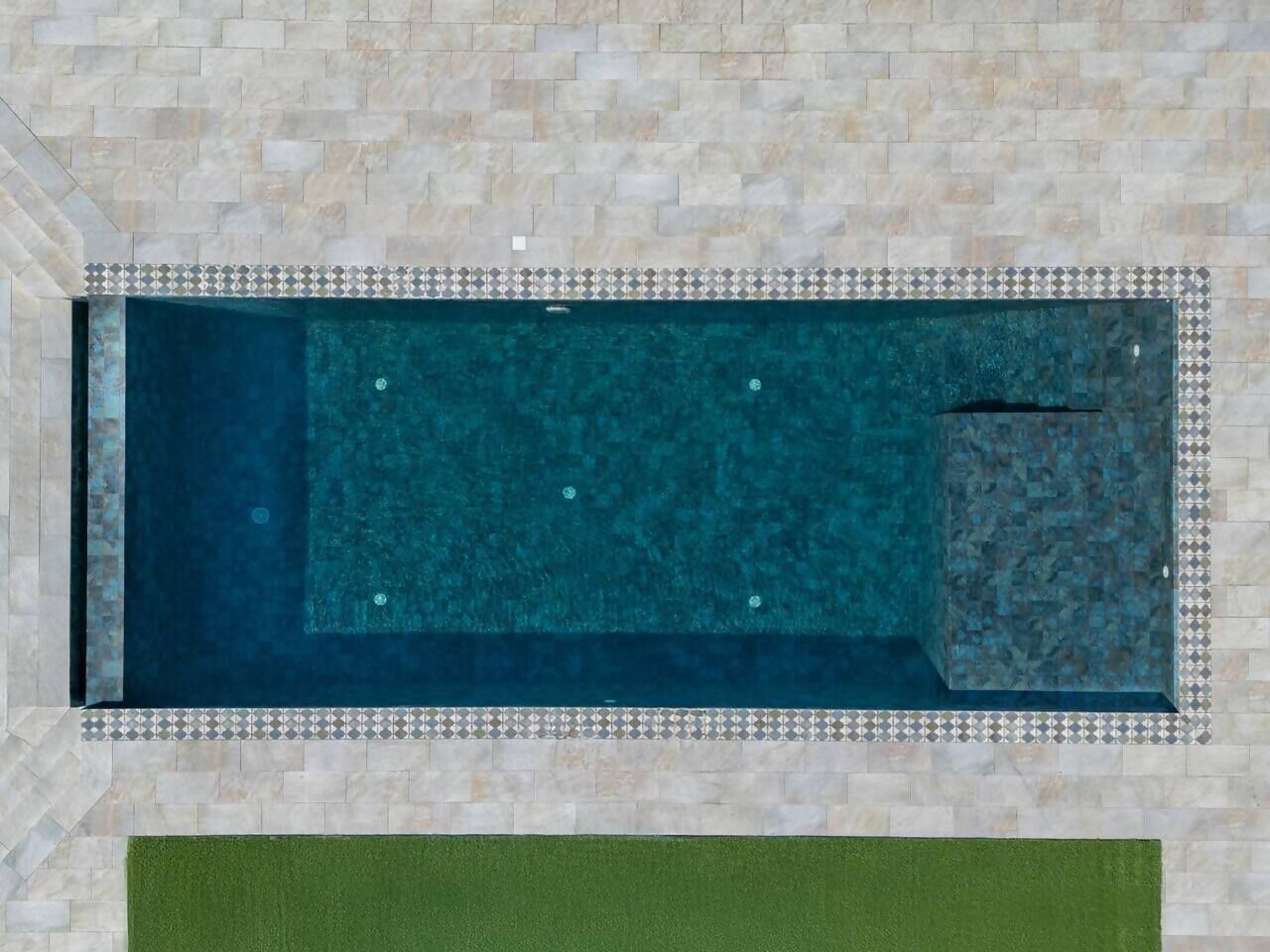A rectangular swimming pool with a tiled border, surrounded by a stone wall.
