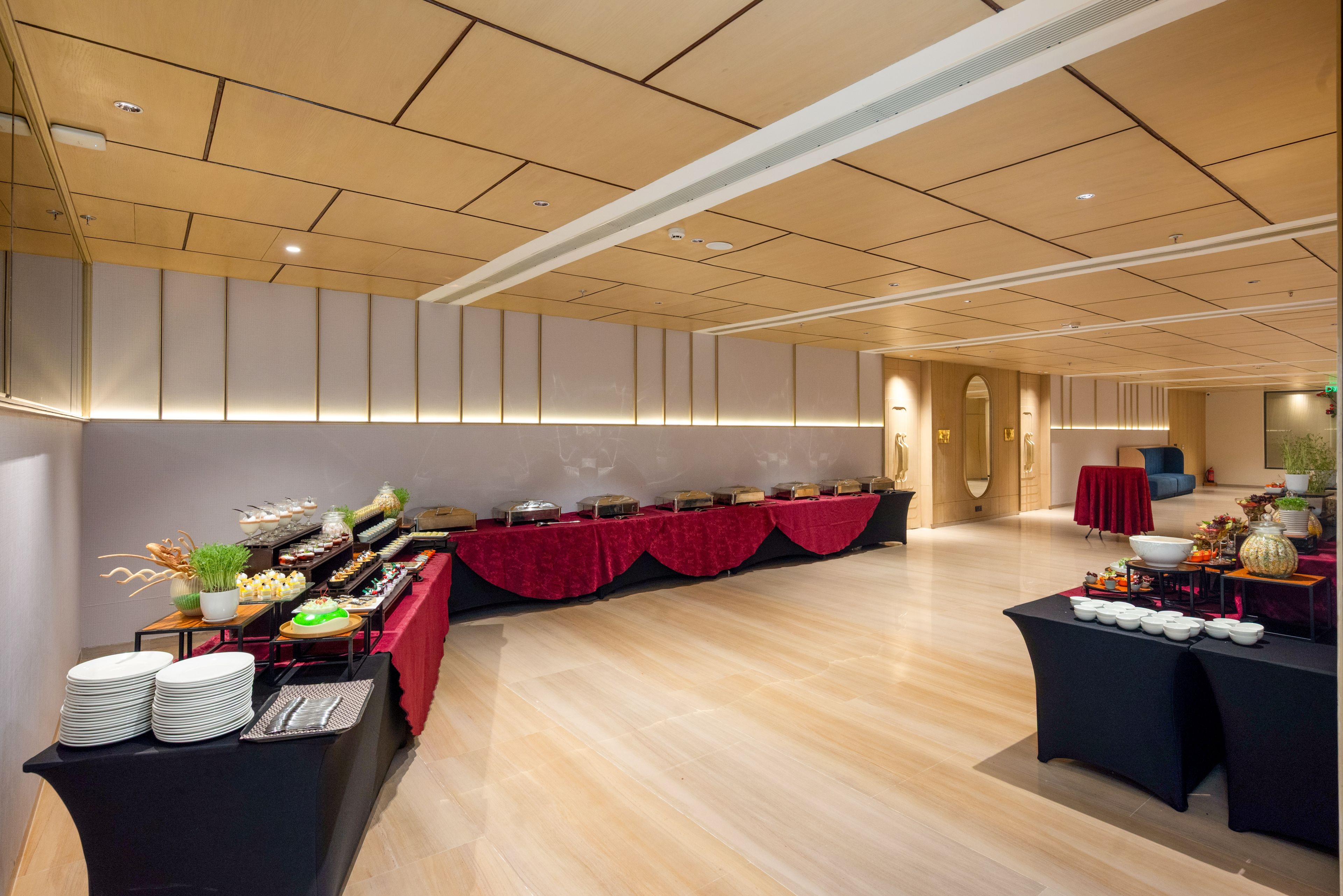 Una habitación amplia con una larga mesa de buffet cubierta con un mantel rojo, una zona de estar con un sofá azul y una pared con un espejo decorativo.