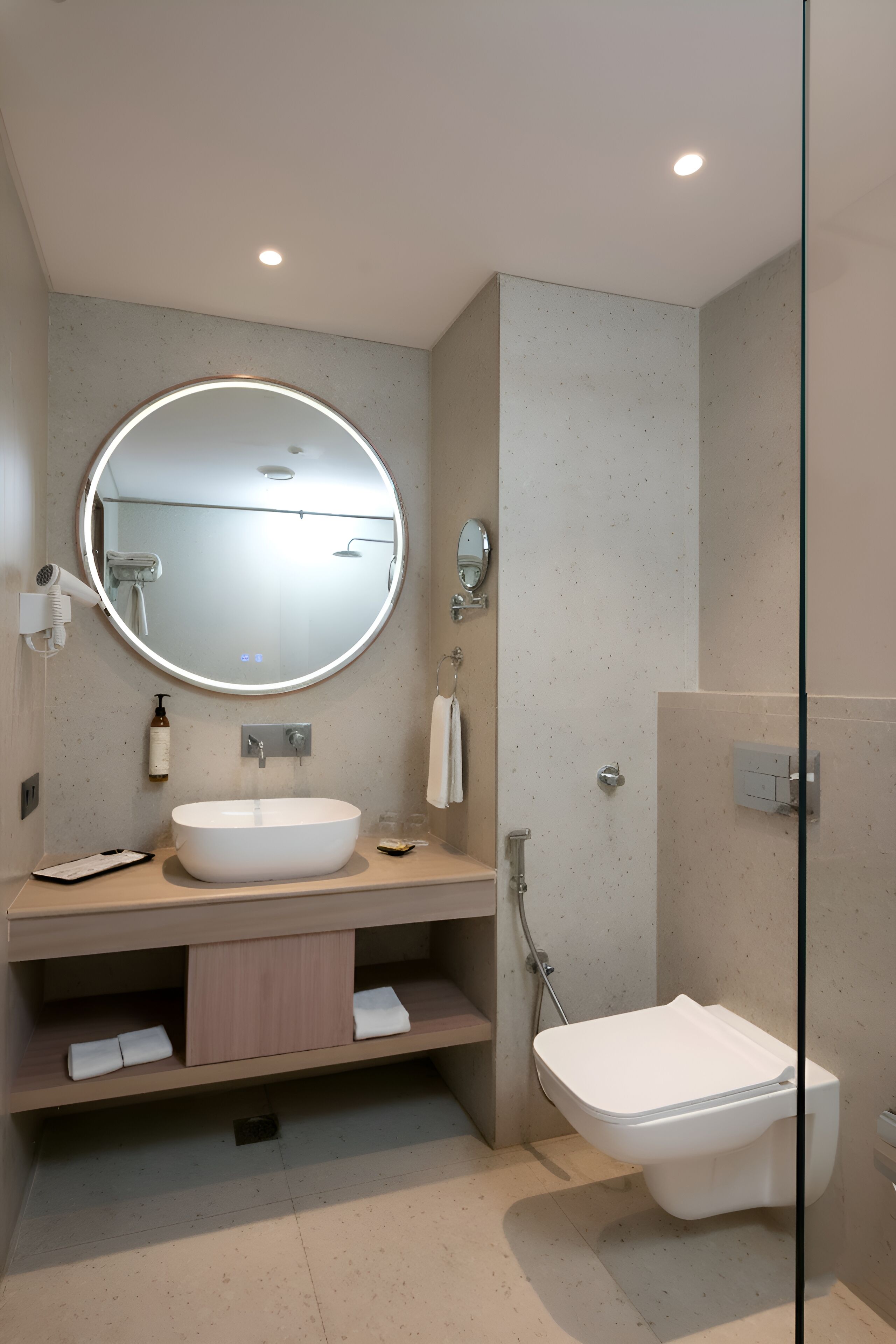 A modern bathroom with a round mirror, a sink, a toilet, and a shower.
