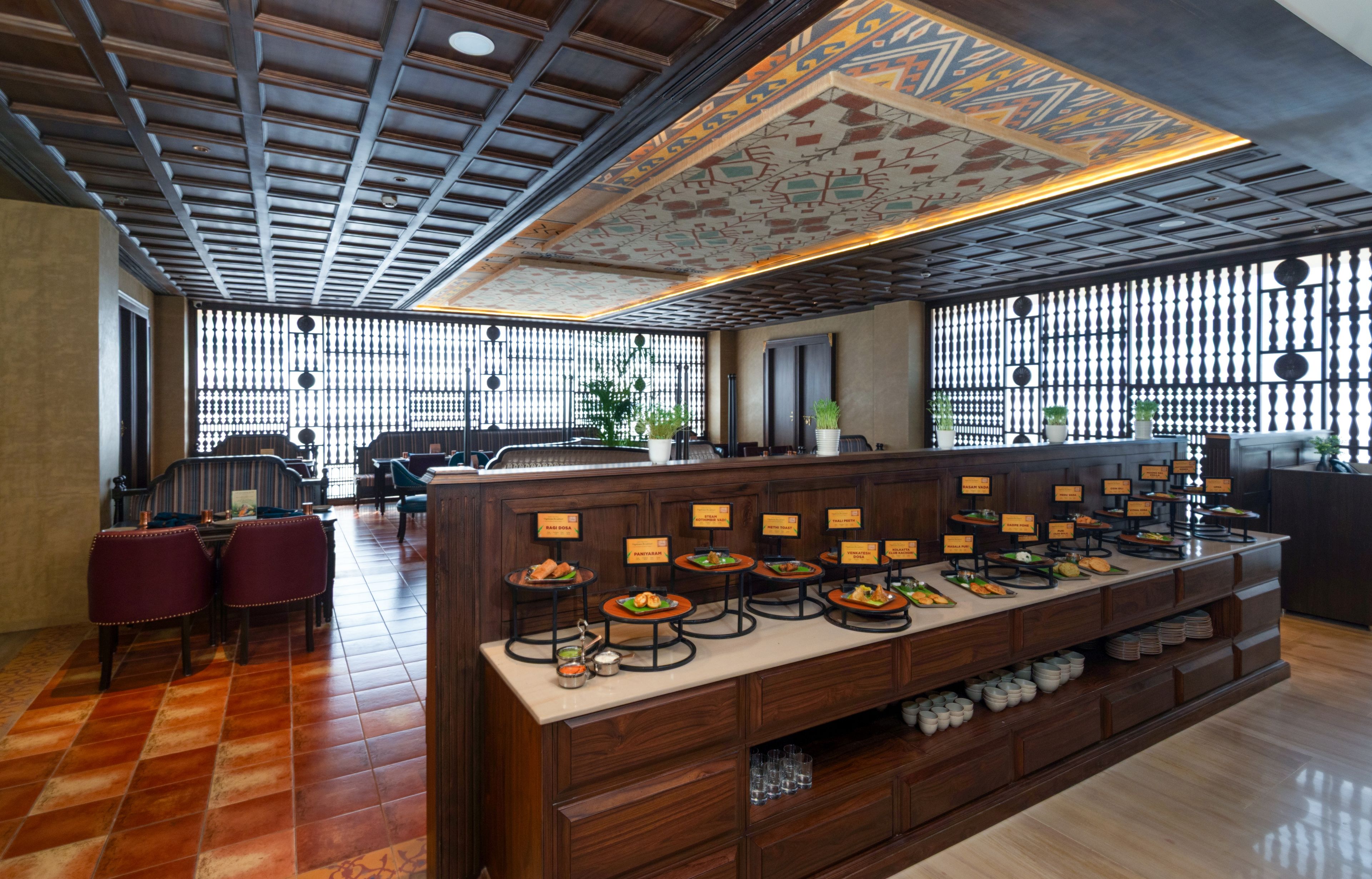 Un restaurante con una larga barra que exhibe diversos platos, techo de madera y pared con diseño.
