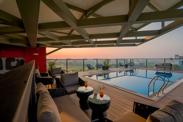A rooftop pool area with lounge seating and a view of the city skyline.
