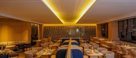 A modern restaurant with high tables and booths, warm lighting, and a central column.