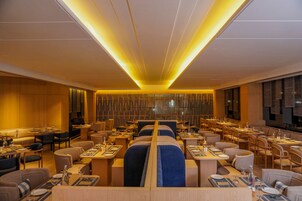 Un restaurante moderno con mesas altas y cabinas, iluminación cálida y una columna central.
