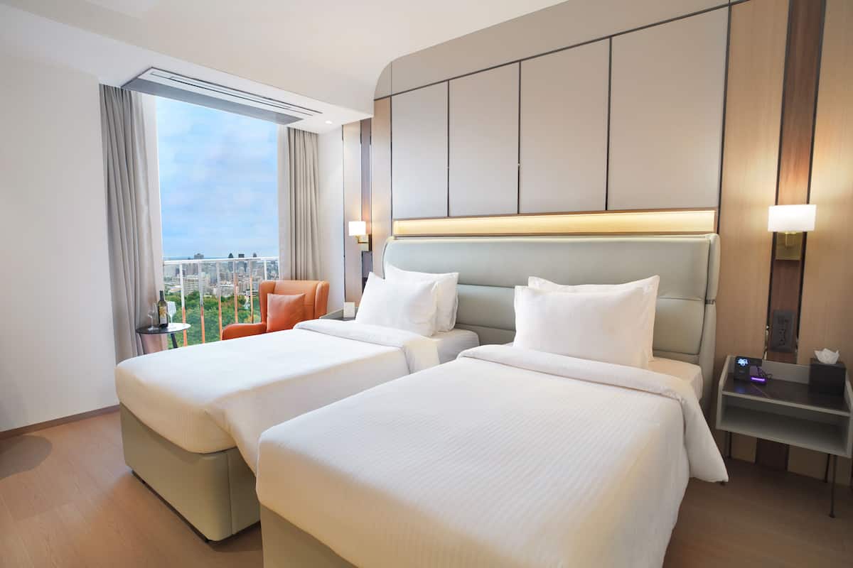 Une chambre d’hôtel avec deux lits, une vue sur la ville, une petite table avec une lampe et une table de chevet avec un téléphone et un chargeur.