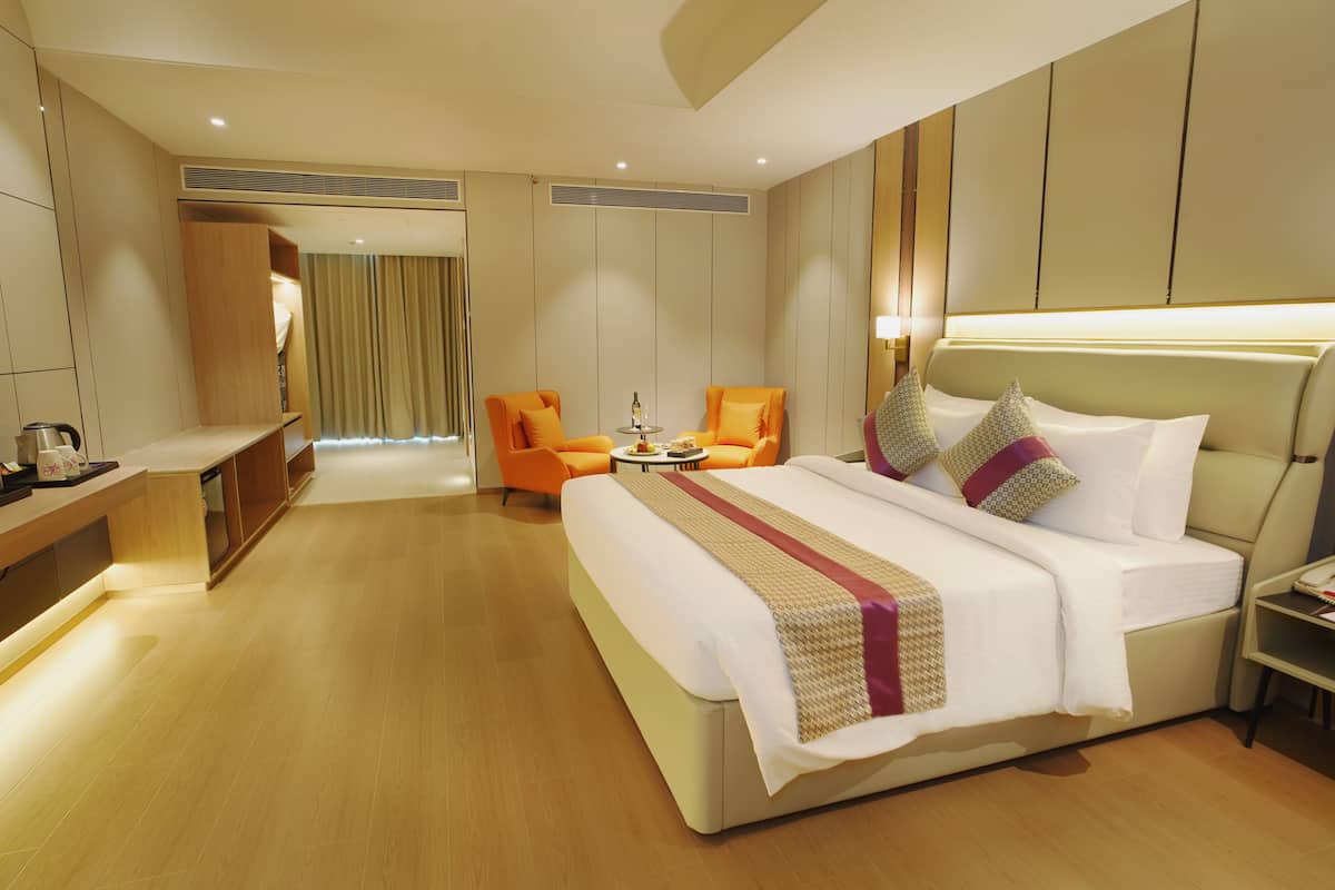 Une chambre d’hôtel moderne, dotée d’un grand lit, de deux fauteuils, d’une petite table et d’un bureau avec une lampe.
