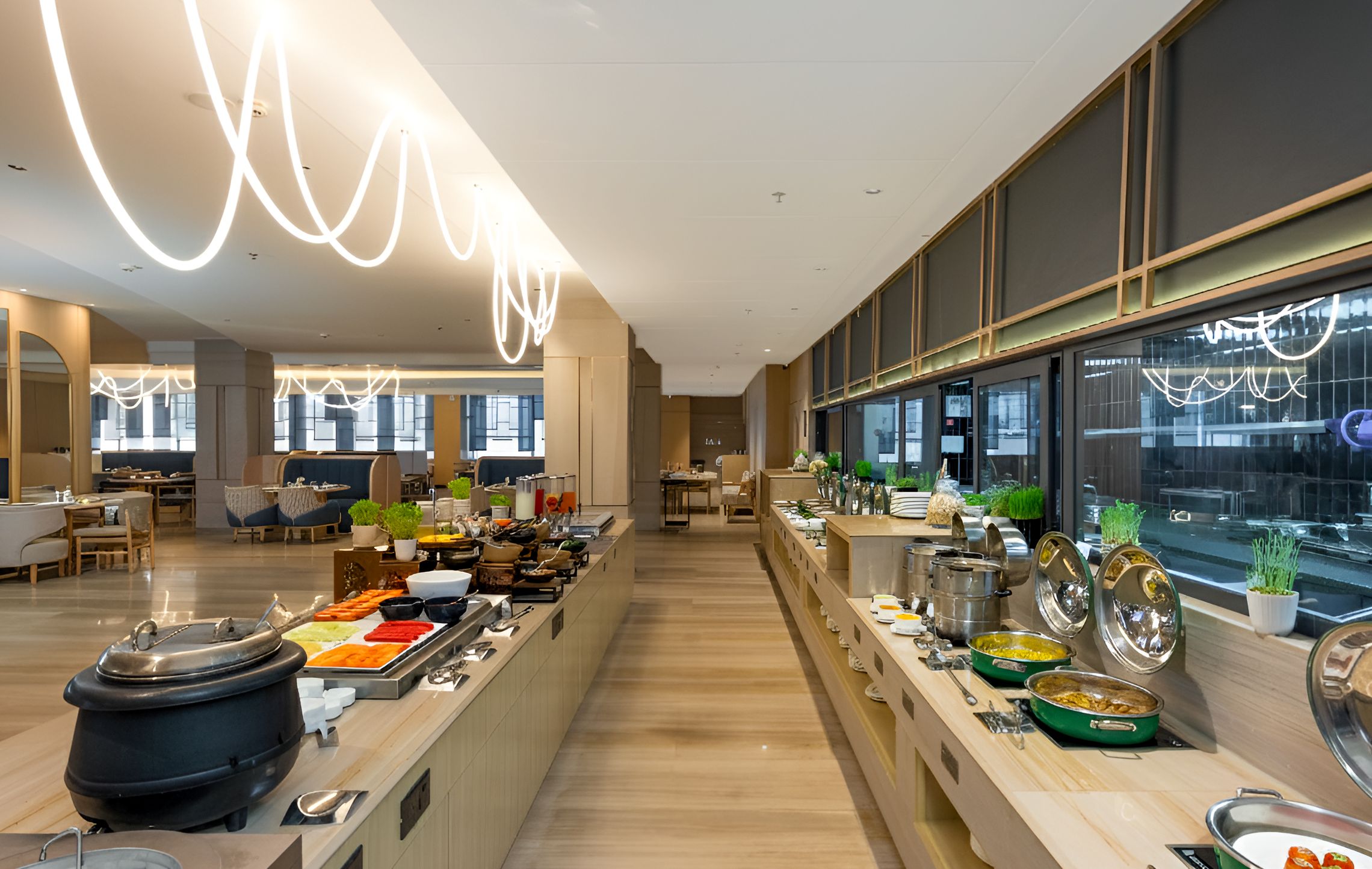 Ein modernes Buffet mit vielfältigen Speisen, ein Sitzbereich mit Tischen und ein großes Fenster mit Ausblick nach draußen.