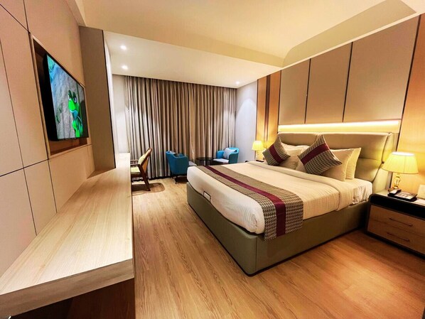 Una habitación de hotel moderna con una cama grande, un televisor en la pared, un escritorio y una zona de estar con sillones.