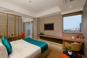 Habitación de hotel moderna con cama, escritorio, televisor y vistas a la ciudad.