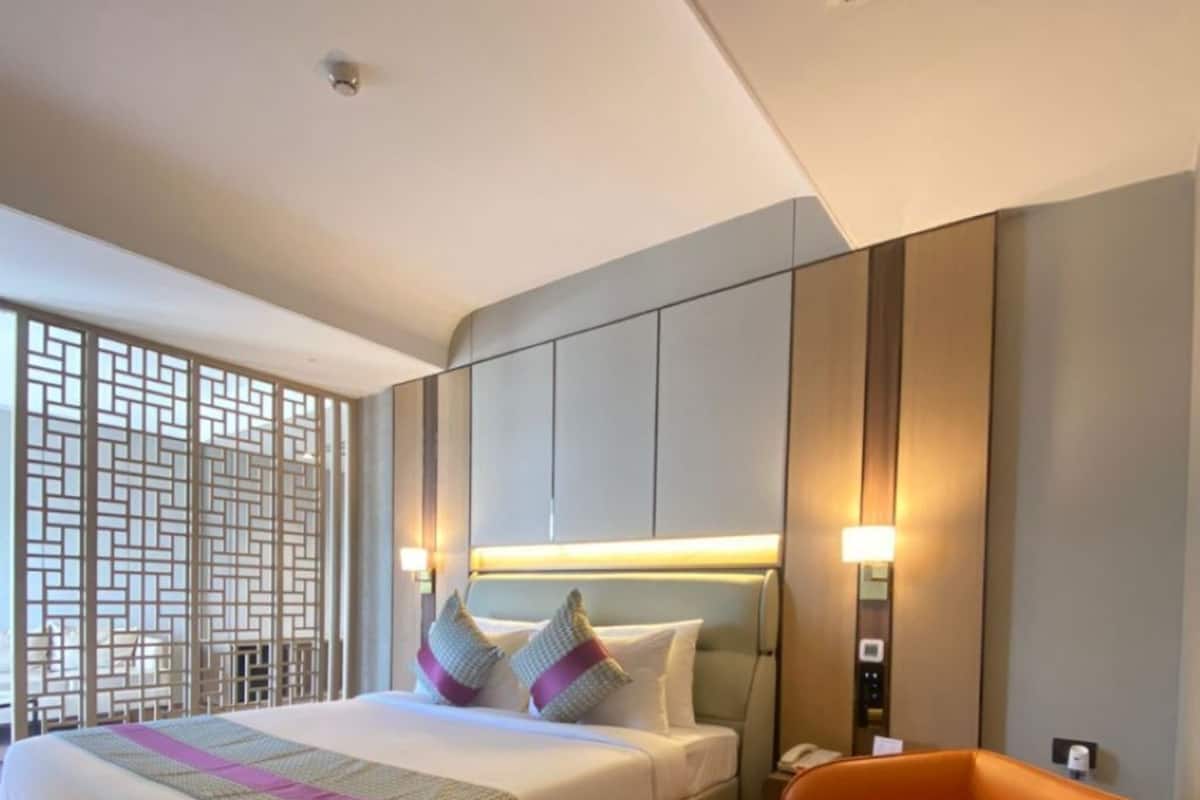 Une chambre d’hôtel moderne dotée d’un grand lit, d’un coin salon et d’une cloison ornée d’un motif géométrique.