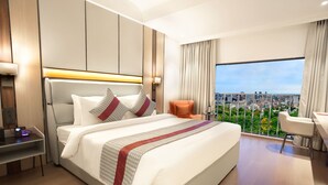 A modern hotel room with a large bed, a desk, and a view of a cityscape. - Orchid Hotel Chandigarh,Zirakpur (Dera Bassi)