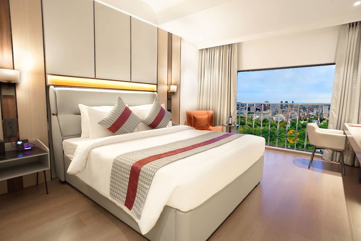 Une chambre d’hôtel moderne, dotée d’un grand lit, d’un bureau et offrant une vue sur le paysage urbain.