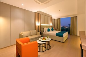 Ein modernes Hotelzimmer mit Bett, Sofa, Couchtisch und Blick auf die Stadt im Abendrot.