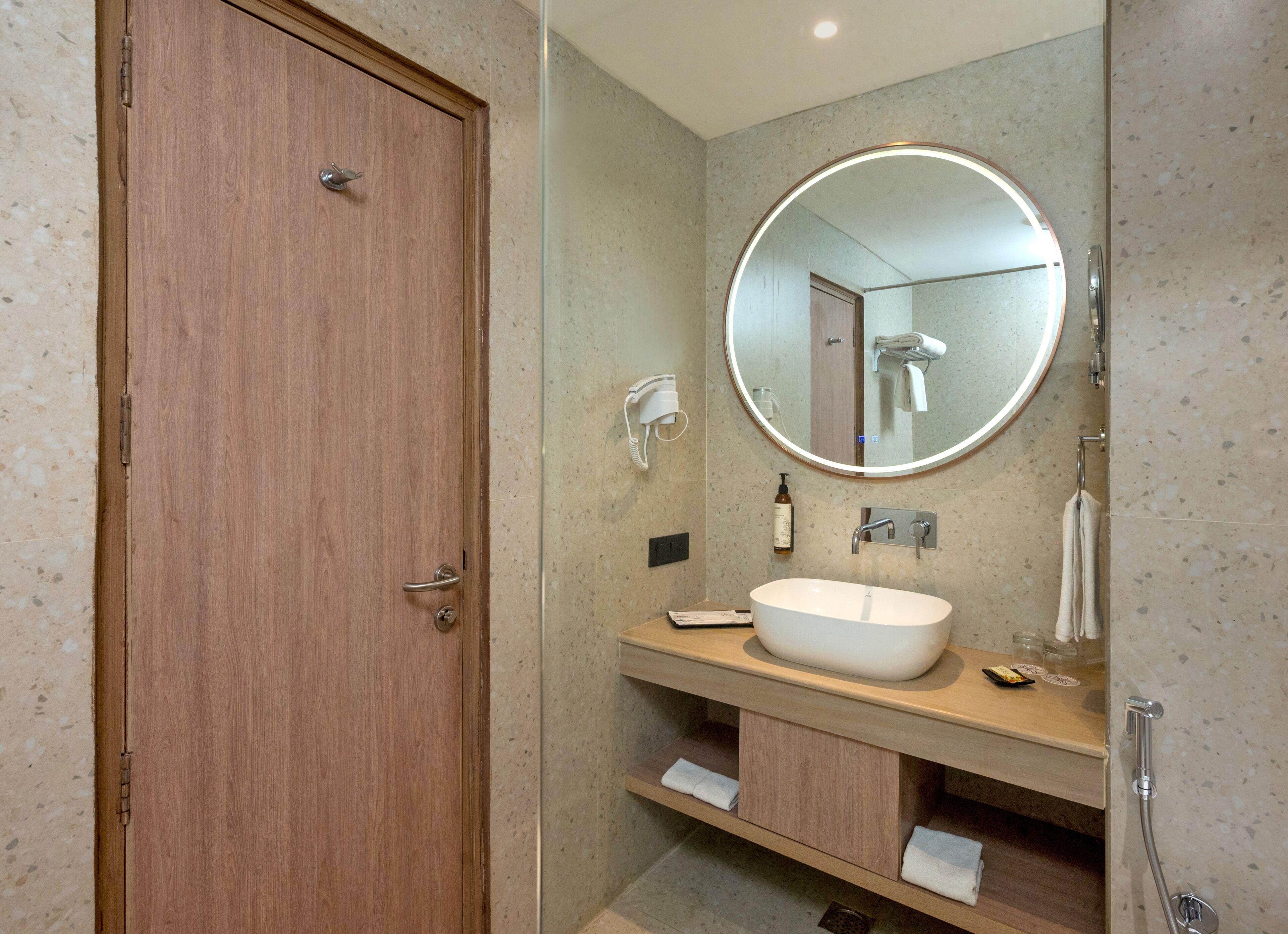A bathroom with a wooden door, a round mirror, a white sink, and a towel rack.