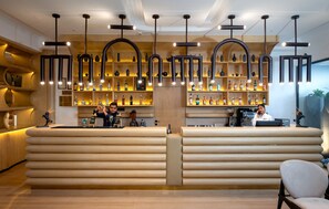 A bar area with a wooden counter, shelves with bottles, and a hanging light fixture.
