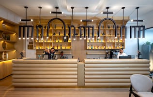 A bar area with a wooden counter, shelves with bottles, and a hanging light fixture.