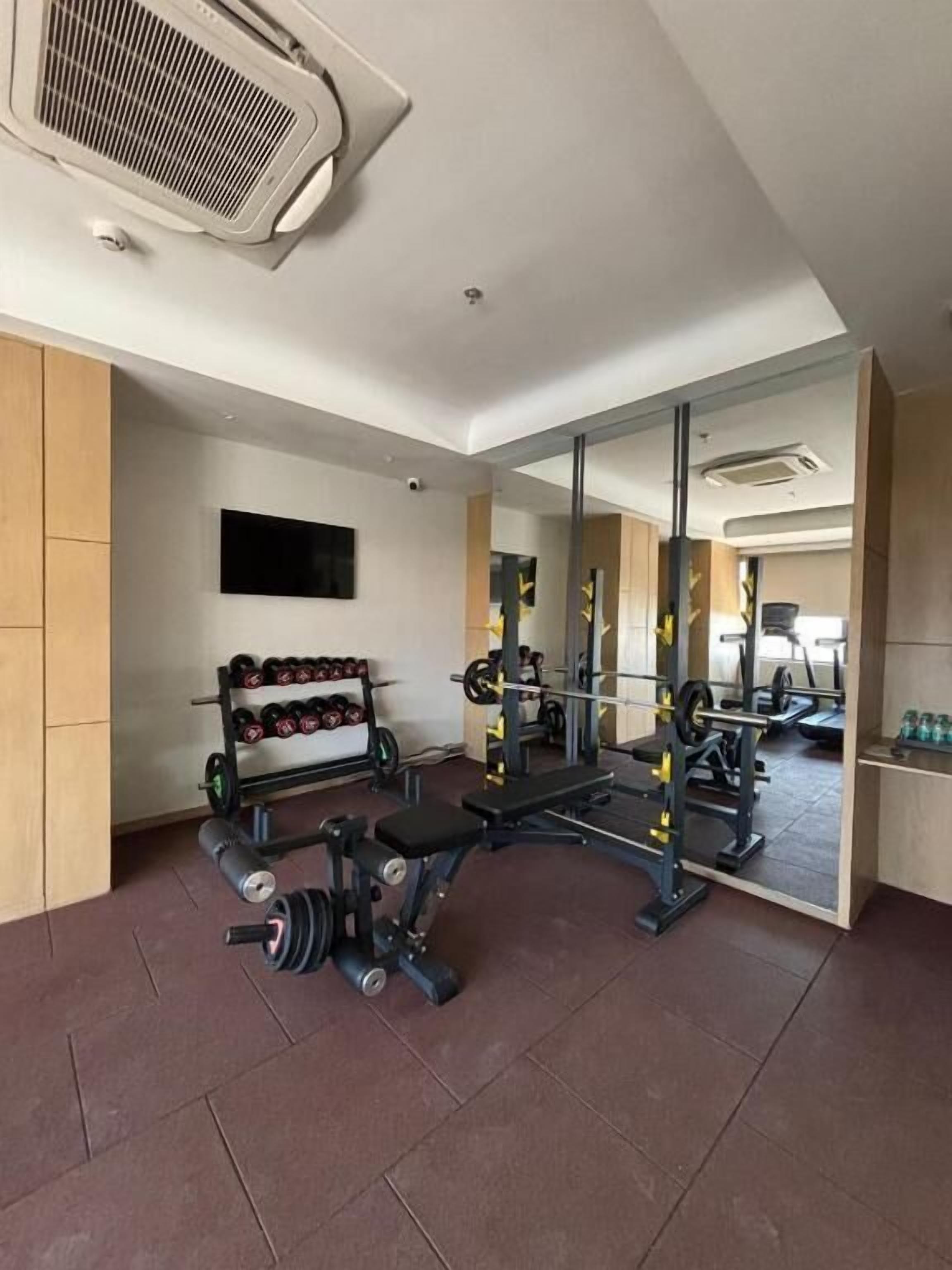A gym with weightlifting equipment, a mirror, and a rack of dumbbells.