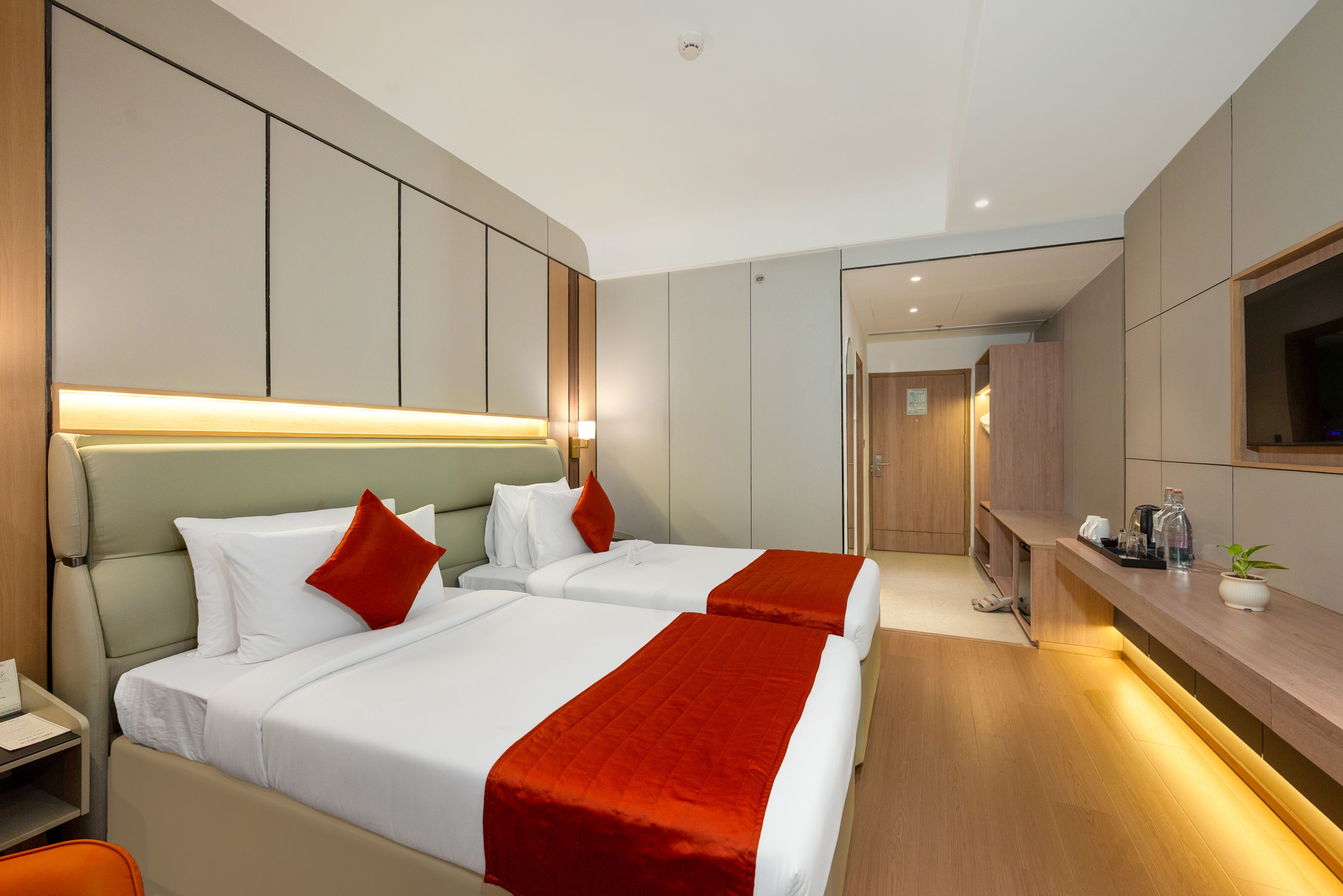 A hotel room with two beds, a desk, a TV, and a bathroom.