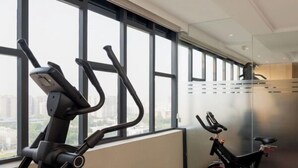 A gym with treadmills, an elliptical, and a stationary bike, large windows, and a polished floor.