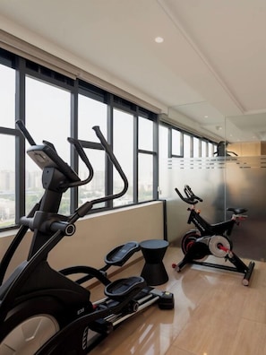 Une salle de sport équipée de tapis de course, d’un vélo elliptique et d’un vélo d’appartement, avec de grandes fenêtres et un sol ciré.
