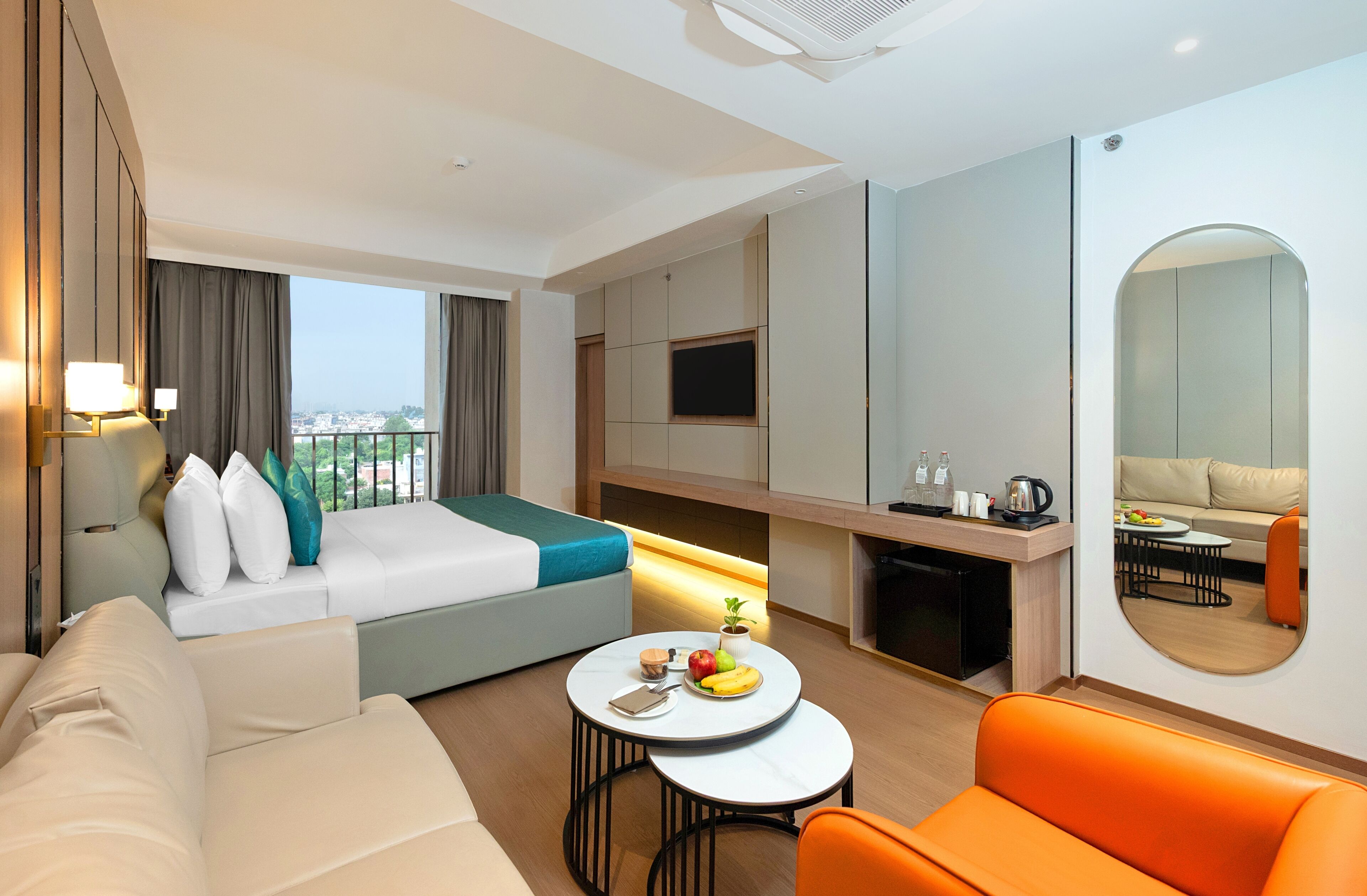 A hotel room with a bed, a sofa, a dining table with fruit, a coffee station, and a TV.