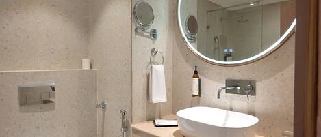 A modern bathroom with a freestanding toilet, a sink with a mirror, and a shower area.
