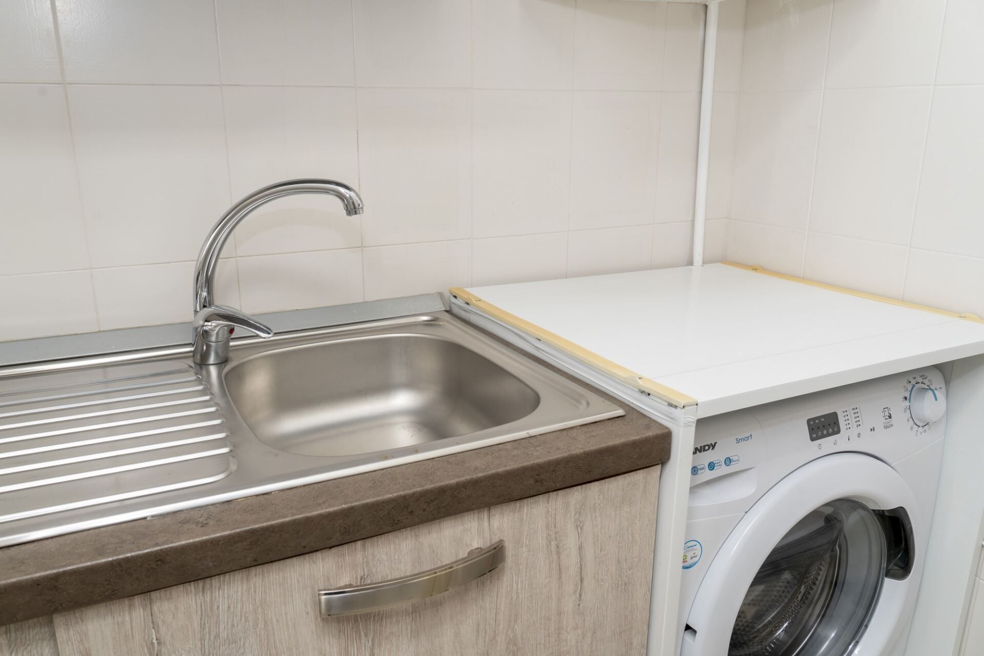 Una cucina con lavello in acciaio inossidabile, piano di lavoro in legno e lavatrice integrata.