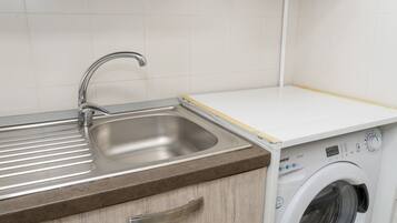 Una cucina con lavello in acciaio inossidabile, piano di lavoro in legno e lavatrice integrata.