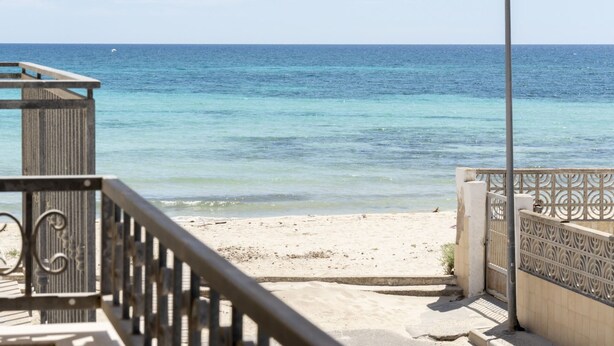 A beach view with a wooden staircase leading down to the sand, a metal railing, and a decorative gate.