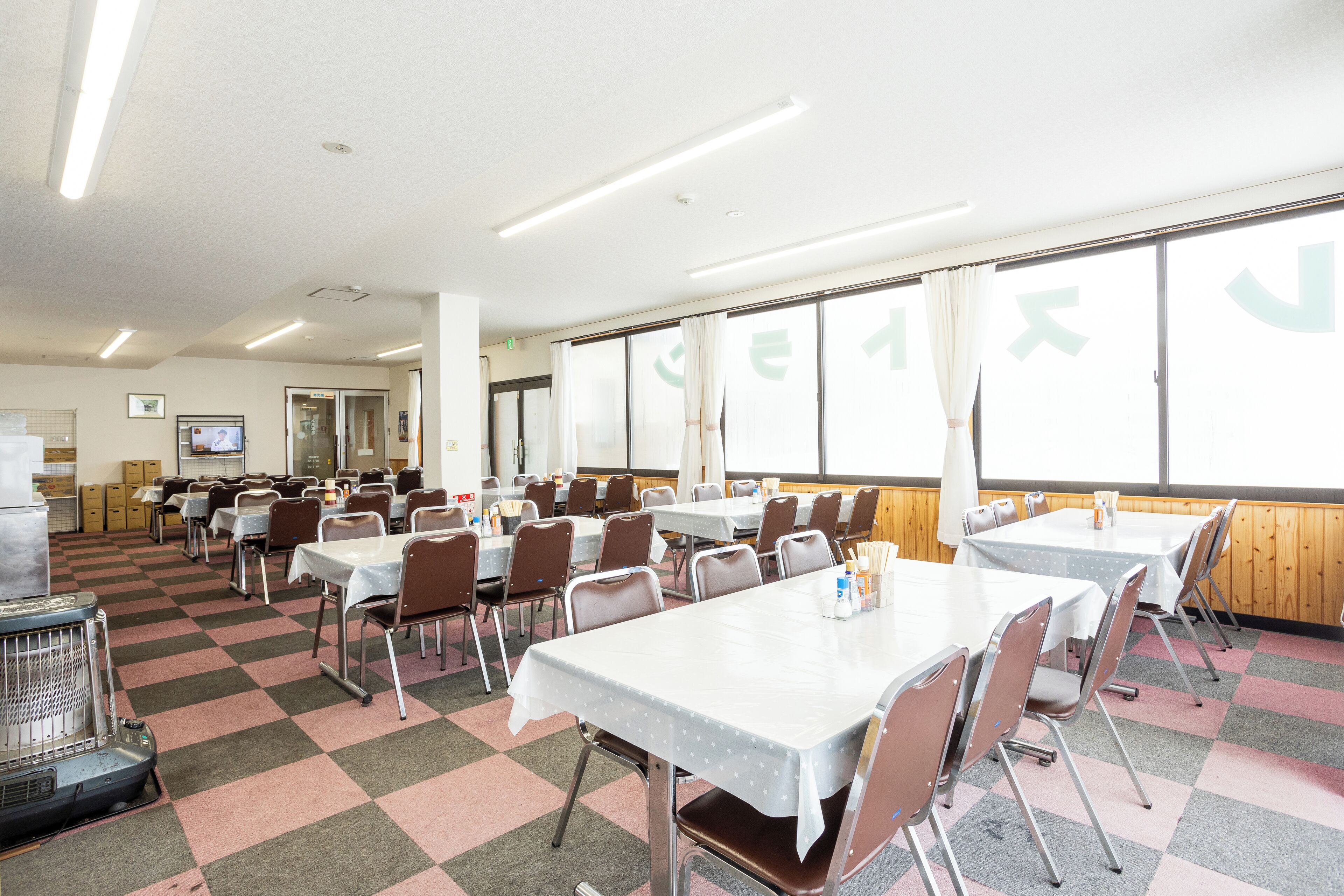 A dining area with tables and chairs, a large window with curtains, and a checkered floor pattern.