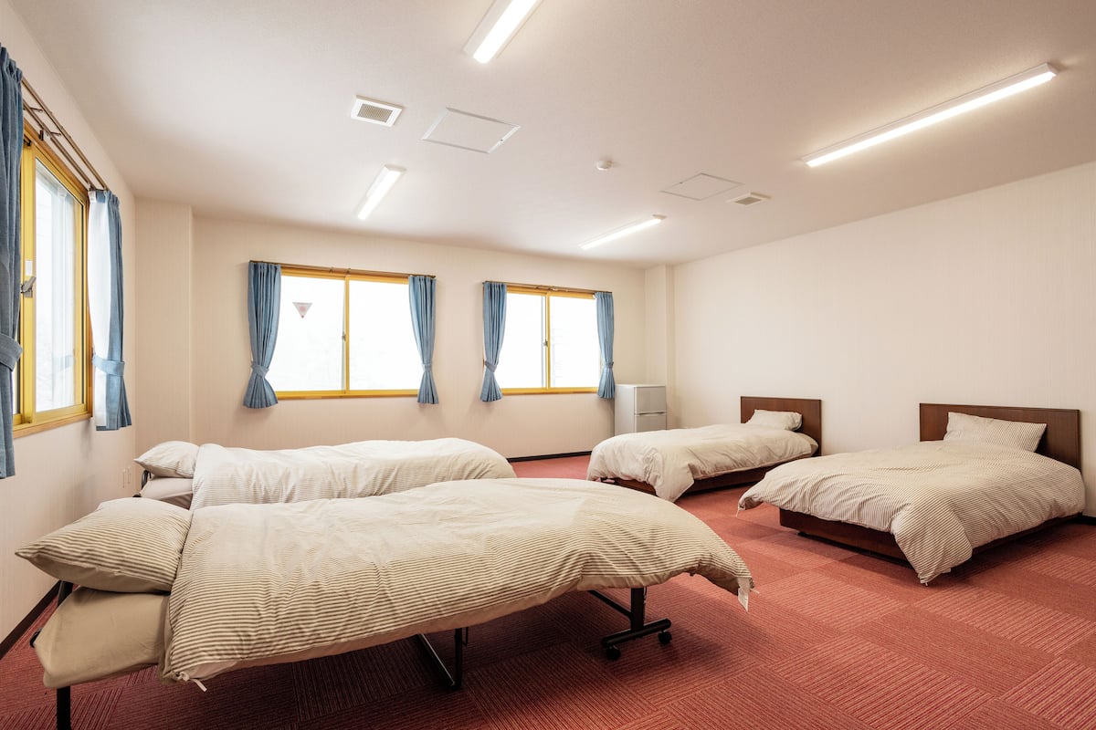 A hotel room with three single beds, a small bedside table, and a window with curtains.