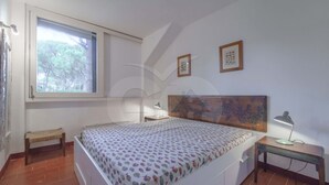 A bedroom with a bed, a desk, a chair, a window, and two framed pictures on the wall.