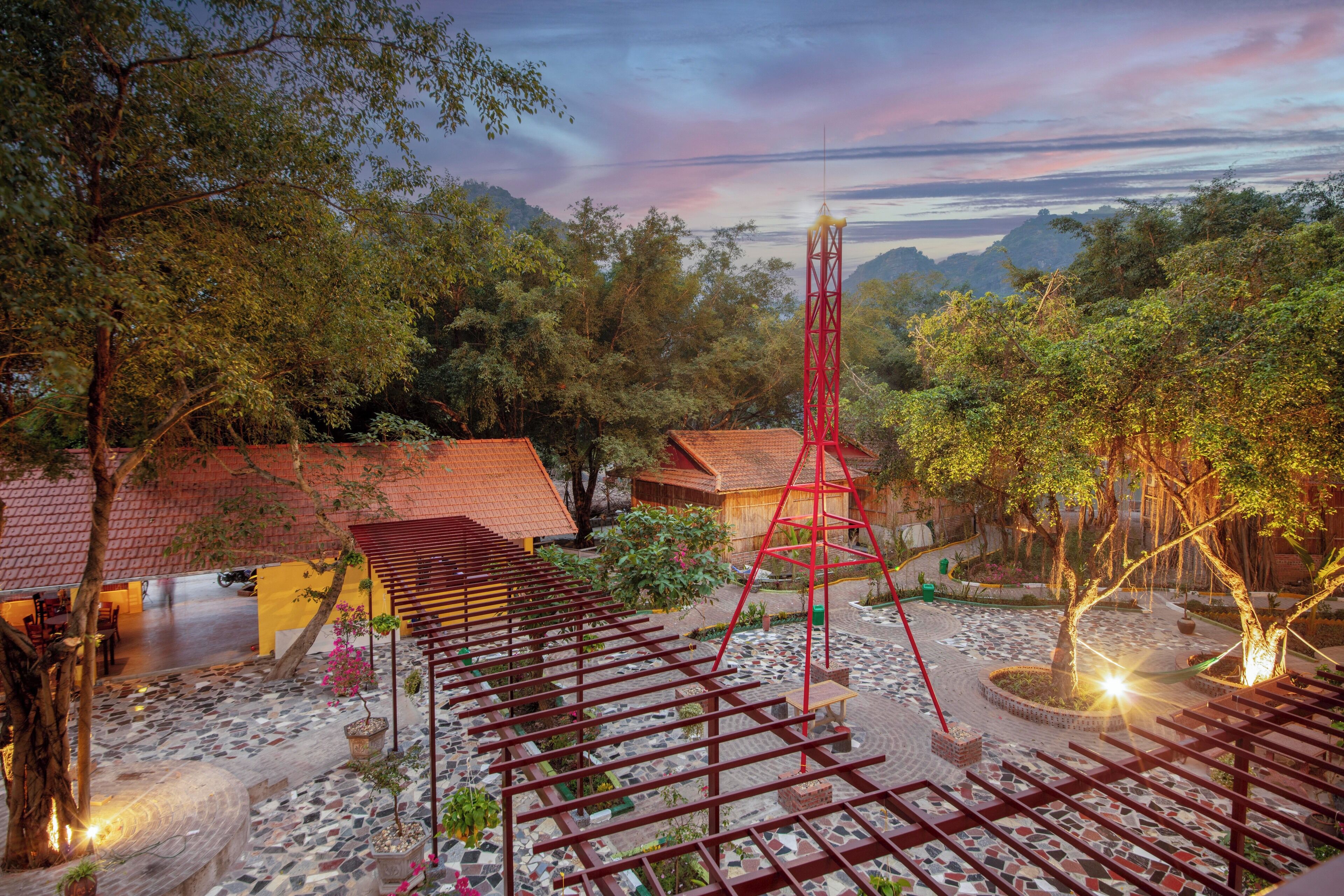 A courtyard with a pergola, a red tower, and traditional buildings.
