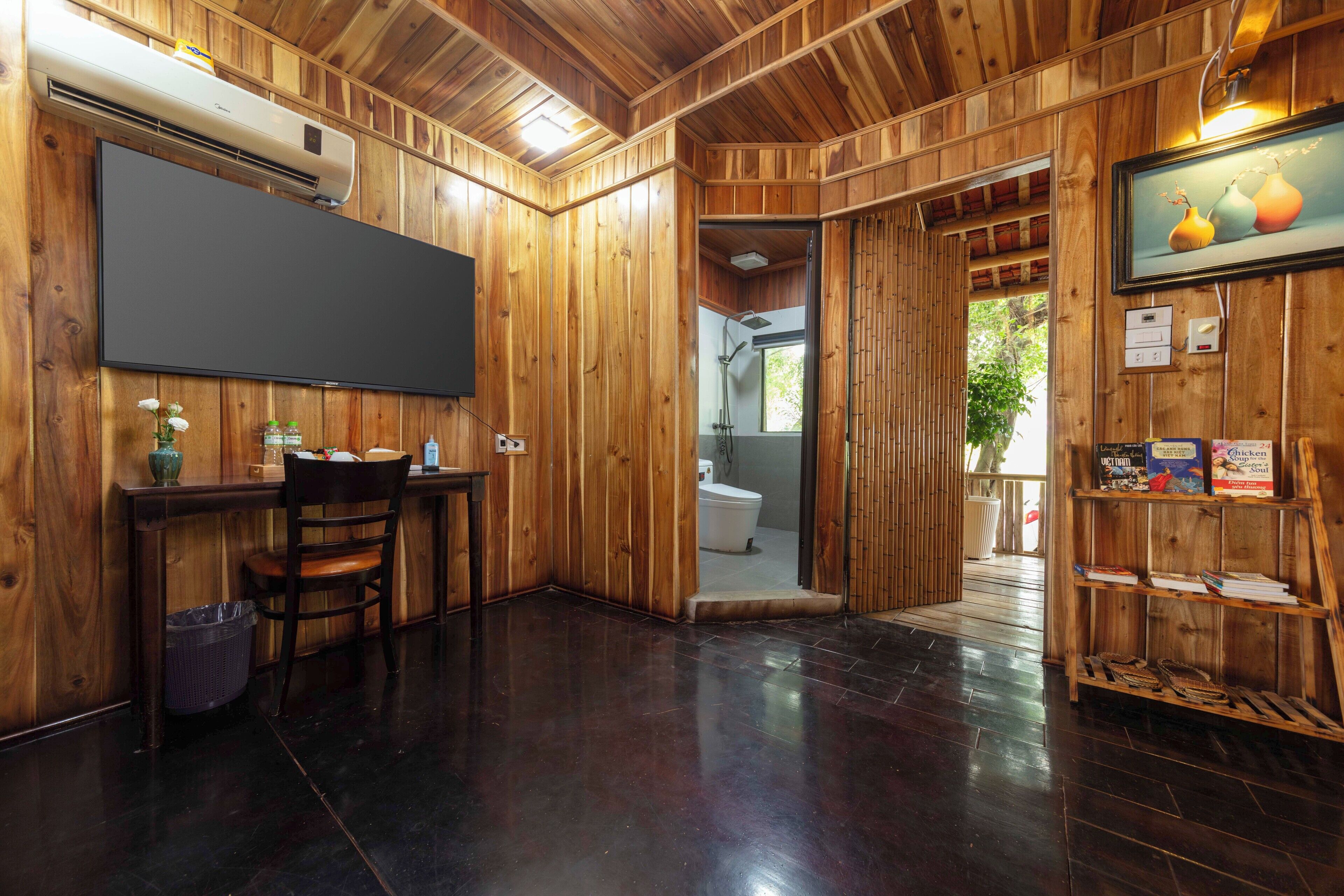 A wooden interior with a flat-screen TV, a chair, a small table, and a bookshelf.