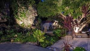A landscaped garden with a paved walkway, a white building, and a large tree with red leaves. - Trang An Ecorest Resort & Spa (Ninh Binh)