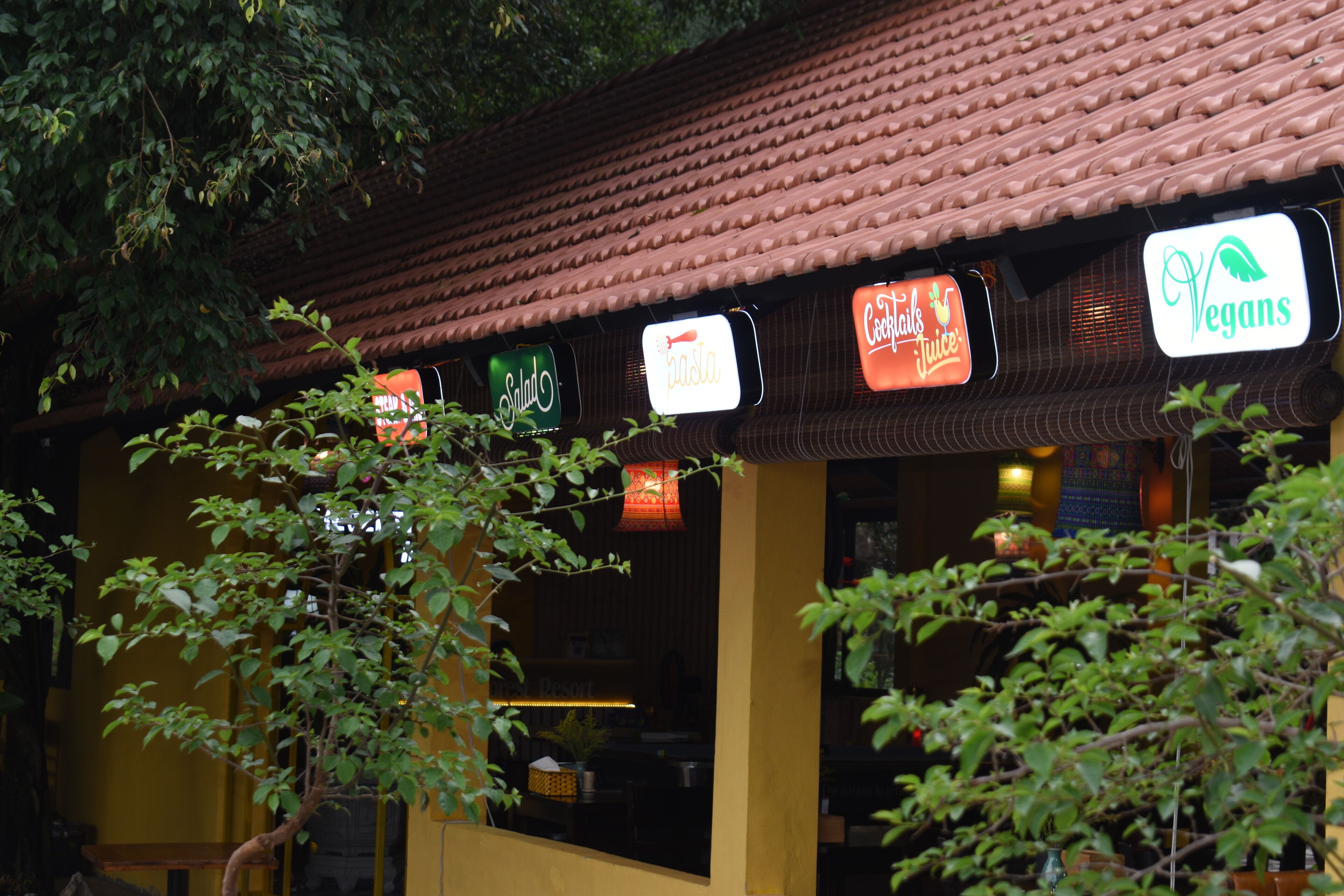 Un ristorante con tetto in tegole e cartelli che indicano 'Pasta', 'Cocacola' e 'Vegani'.